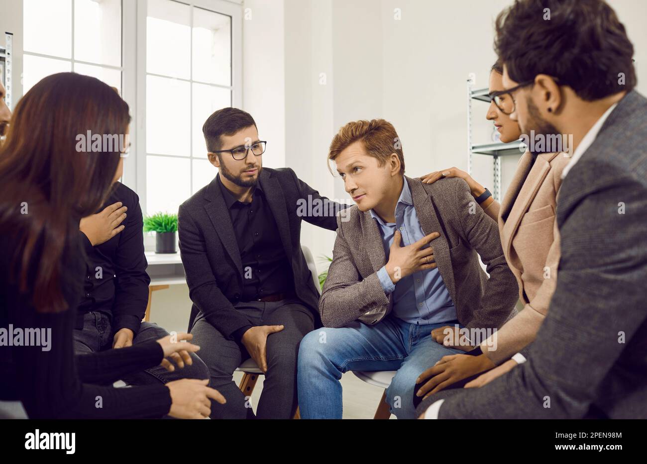 Seitlicher Blick auf eine Gruppe versammelter Leute, die ihren Kameraden trösten, indem sie ihre Hand auf seine Schulter legen. Stockfoto