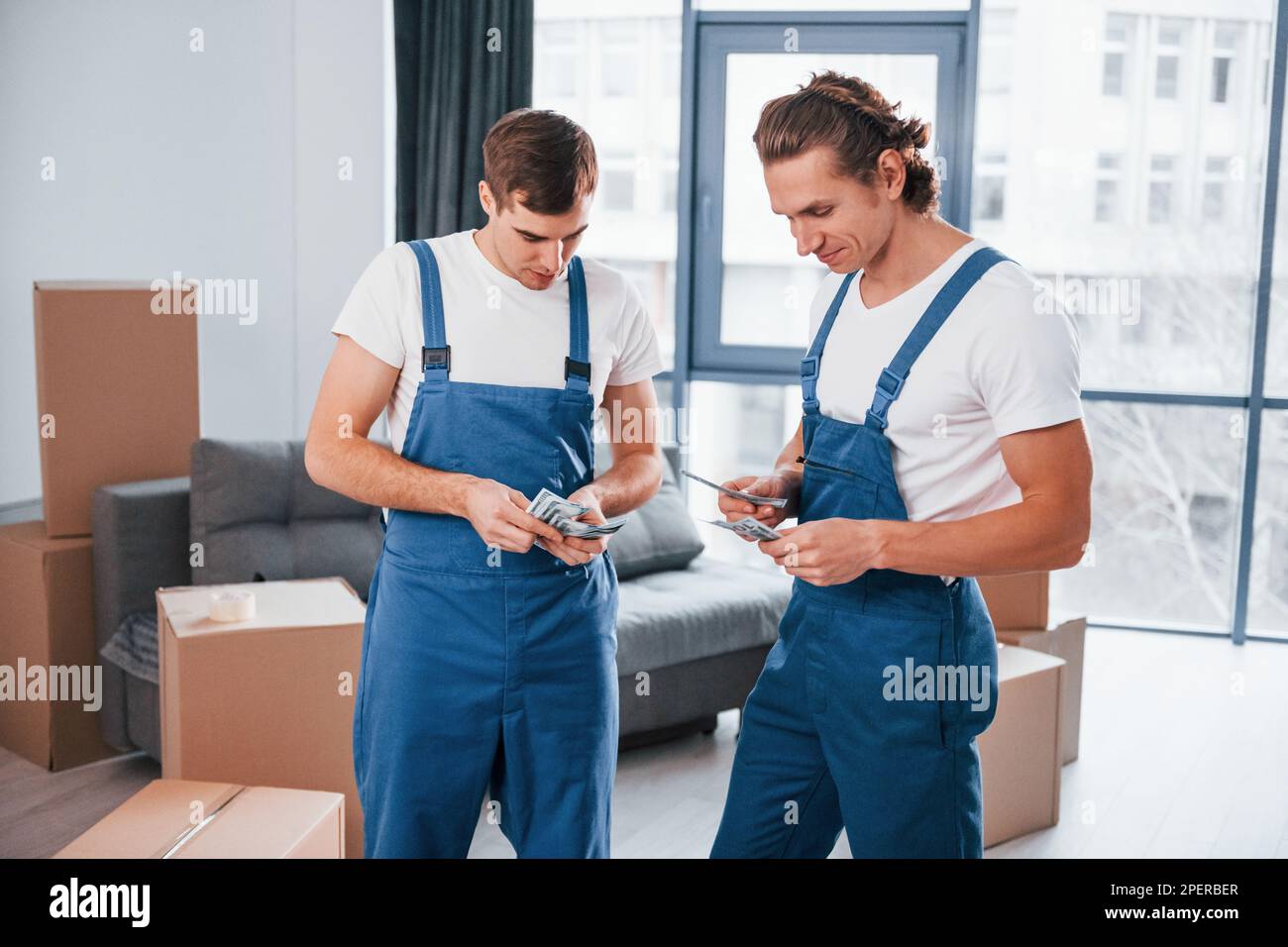 Ich habe Geld. Zwei junge Spielfiguren in blauer Uniform, die im Zimmer arbeiten Stockfoto