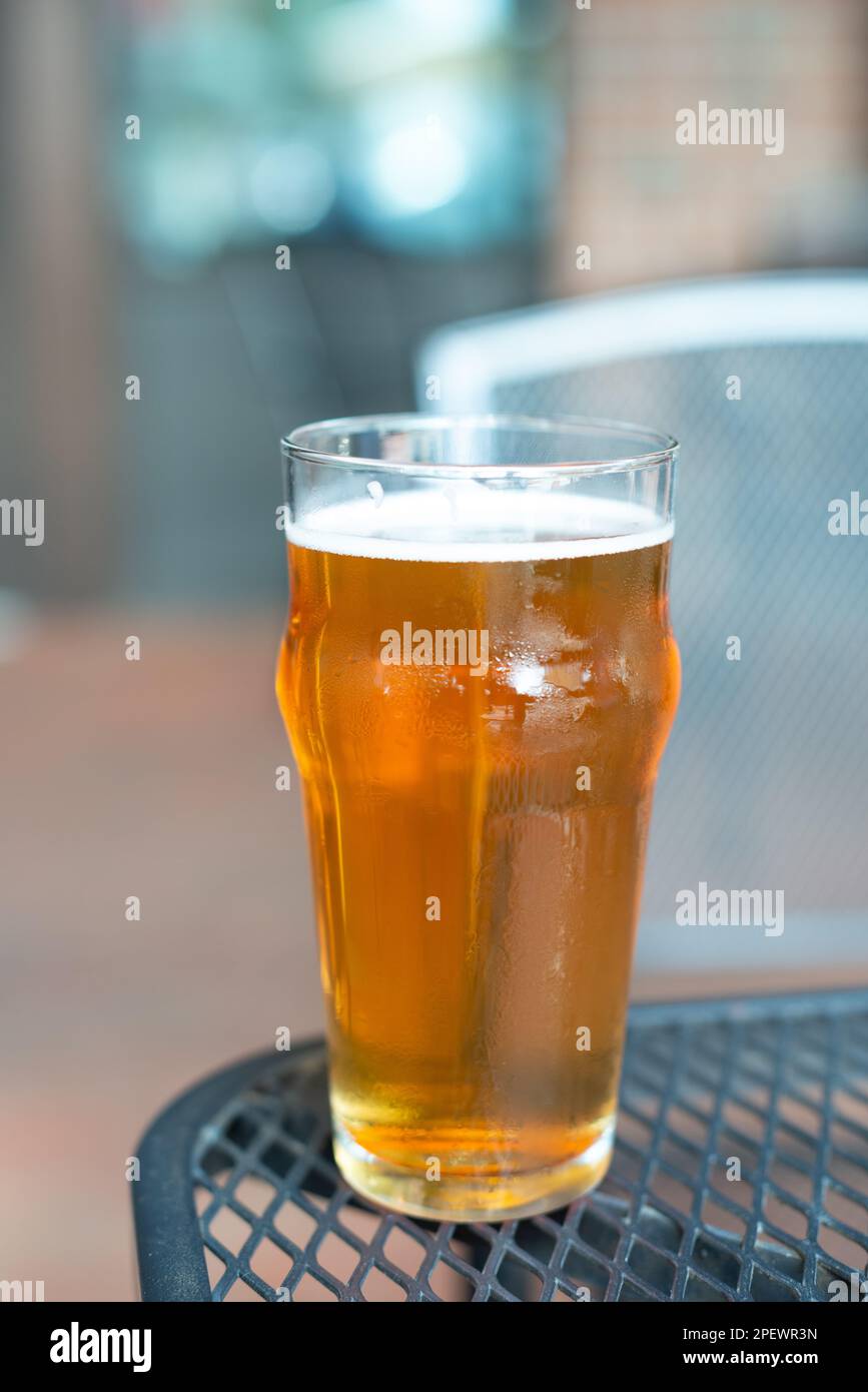 Ein Glas indisches, helles Craft-Bier mit weißem Schaum auf dem Kopf. Die goldene Flüssigkeit besteht aus einem orangefarbenen Bier in einem hohen, klaren Pint-Glas. Stockfoto