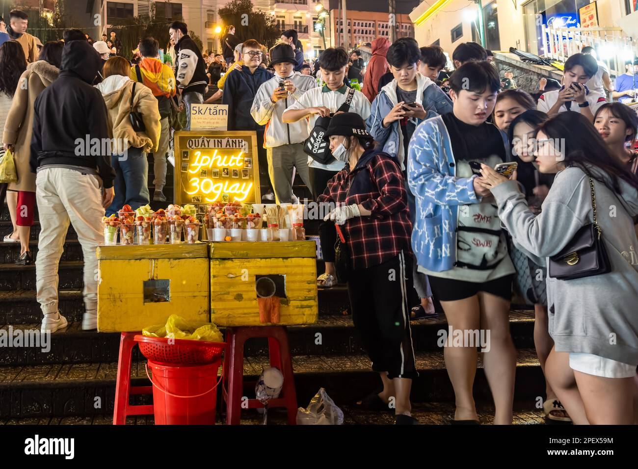 Auf den Stufen im Zentrum von Dalats Nachtmarkt in Vietnam treffen sich junge Gruppen von Freunden, um nachts auf ihre Mobiltelefone zu schauen. Stockfoto