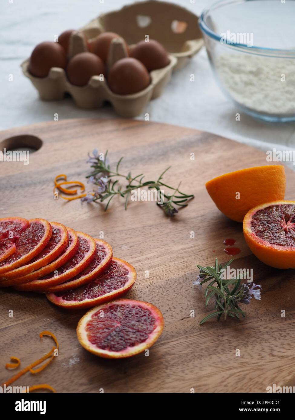 Nahaufnahme der Backzutaten auf einem Tisch, einschließlich Blutorangen, Rosmarin, Mehl und Eier zur Zubereitung eines hausgemachten Kuchen Stockfoto