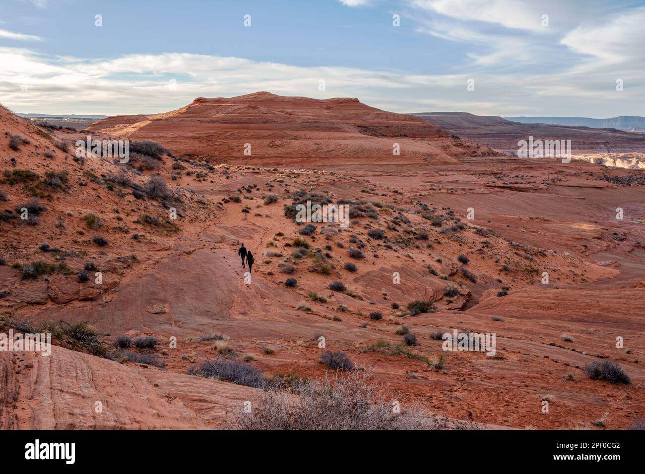 Zwei Menschen, dunkle Figuren, wandern auf dem roten Sandstone Hanging Garden Trail im Glen Canyon National Recreation Area bei Page, Arizona, USA, Stockfoto