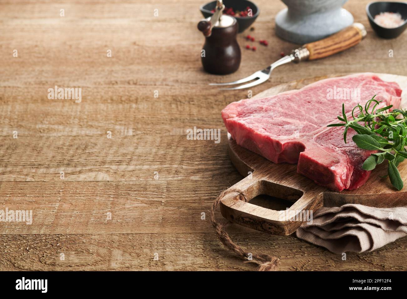 Dickes rohes T-Bone Steak. Trocken gereiftes rohes T-Bone- oder Porterhouse-Rindfleisch-Steak mit Kräutern und Salz auf dunklem Hintergrund. Selektiver Fokus und Kopierbereich. Stockfoto
