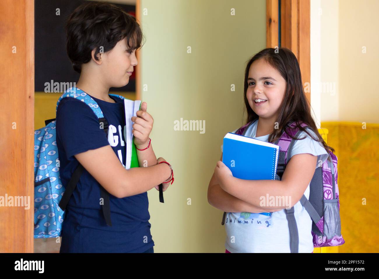 Ein Junge, der vor dem Klassenzimmer mit einem Mädchen redet. Glückliche weiße Grundschulkinder. Junge Schüler, die sich unterhalten. Stockfoto