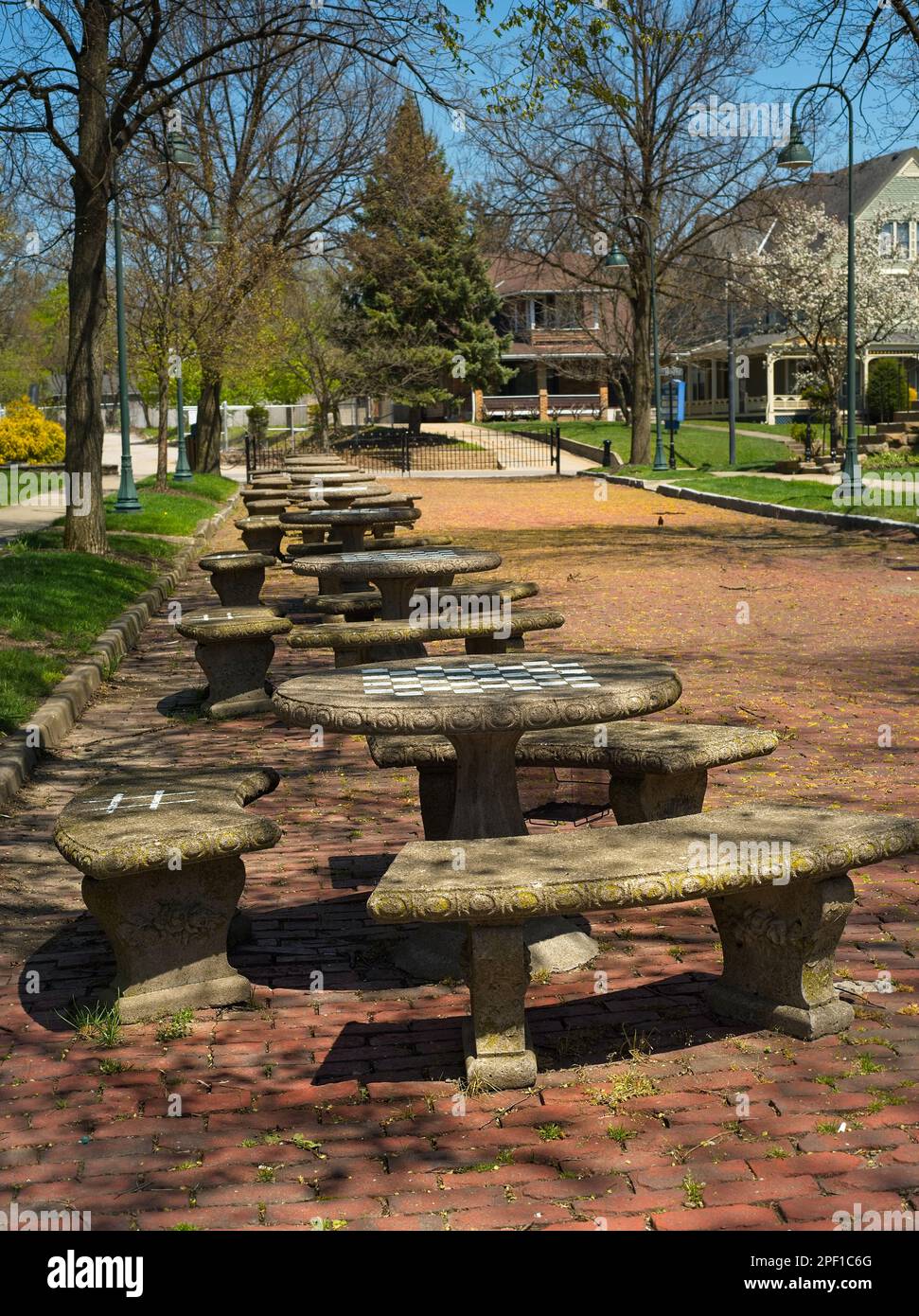 Eine Reihe von Steintischen befindet sich in einer alten Backsteinstraße neben einem Gemeindehaus in Ohio. Auf jedem Tisch befindet sich ein Schachbrett für Schach oder ein Schachbrett Stockfoto