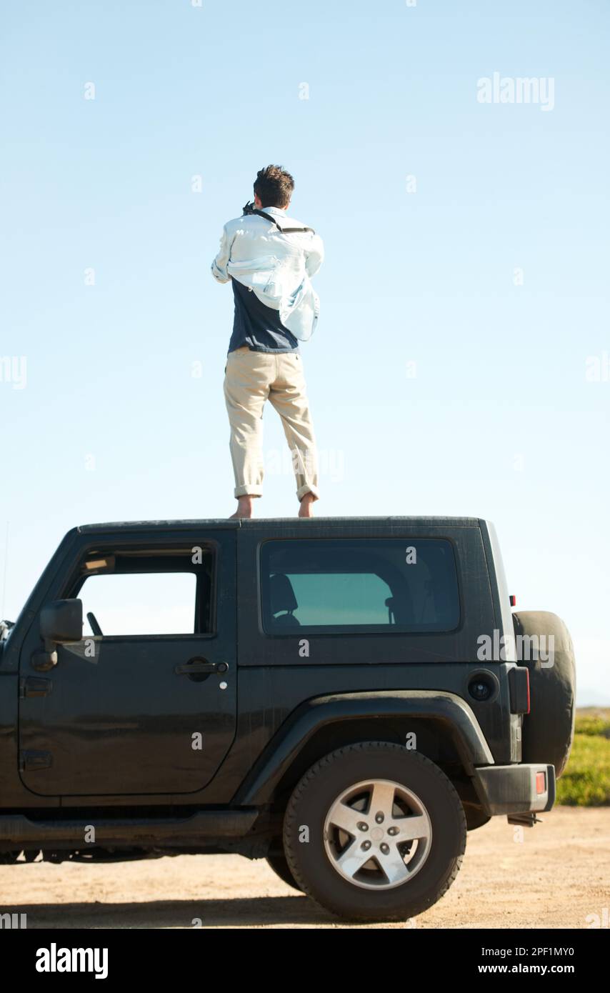 Ich muss höher. Ein junger Mann, der für eine bessere Aussicht ins Auto steigt. Stockfoto