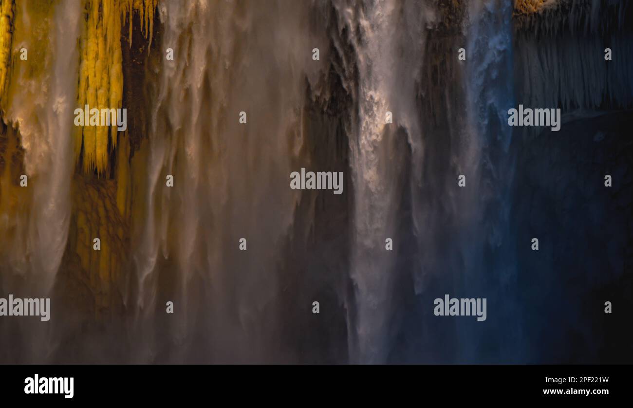 Details von Stalagmiten und Wasser, das aus dem Skógafoss-Wasserfall in Island fällt, erleuchtet durch das abendliche Sonnenlicht und schafft eine märchenhafte Atmosphäre wie Stockfoto