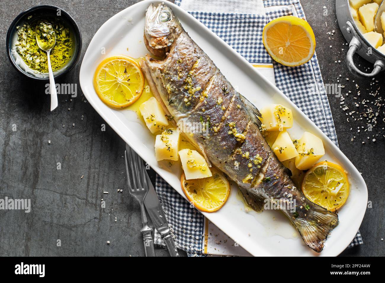 Gebratene traditionelle Flusforelle mit Salat, Kartoffeln und (Knoblauch, Petersilie) Sauce auf grauem Tischhintergrund Stockfoto