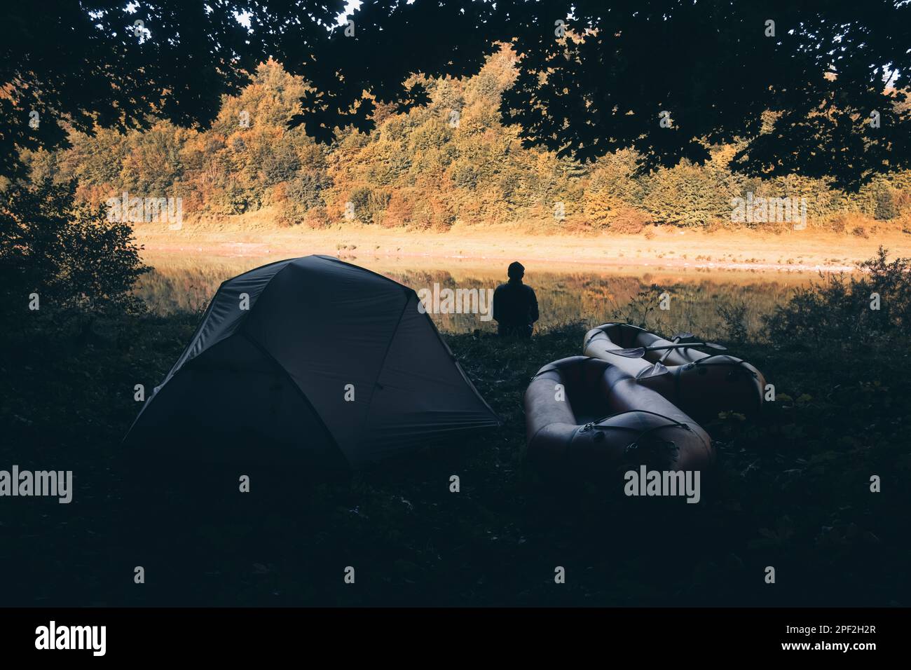 Ein Mann in der Nähe seines Zelts und packrafts in einem Waldlager am Fluss. Packrafting und Konzept der aktiven Lebenszeit Stockfoto