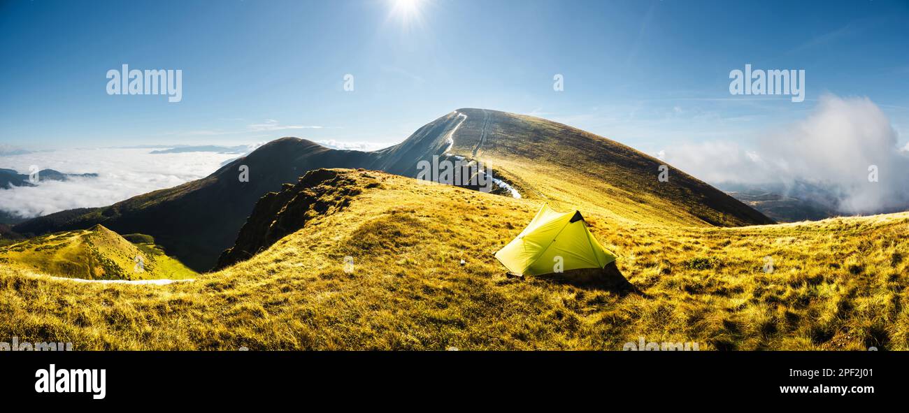 Einsames gelbes Zelt vor der Kulisse einer unglaublichen Berglandschaft bei Sonnenaufgang am Morgen. Tourismuskonzept. Panoramaausrichtung Stockfoto