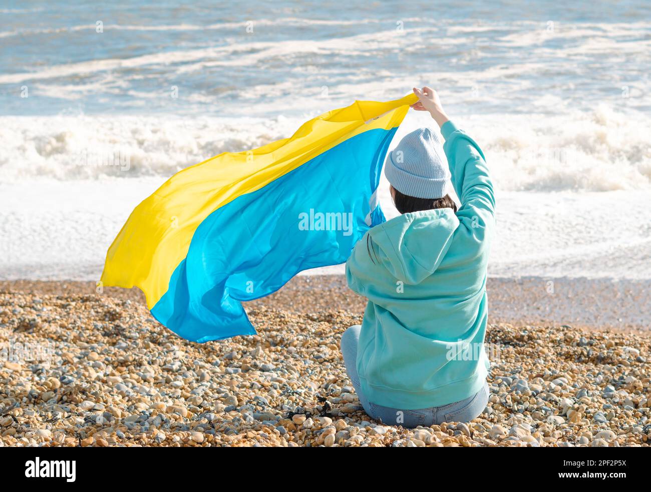 Braune Frau in blauem Hoodie und blauem Hut mit ukrainischer Nationalflagge, patriotisches Konzept Stockfoto