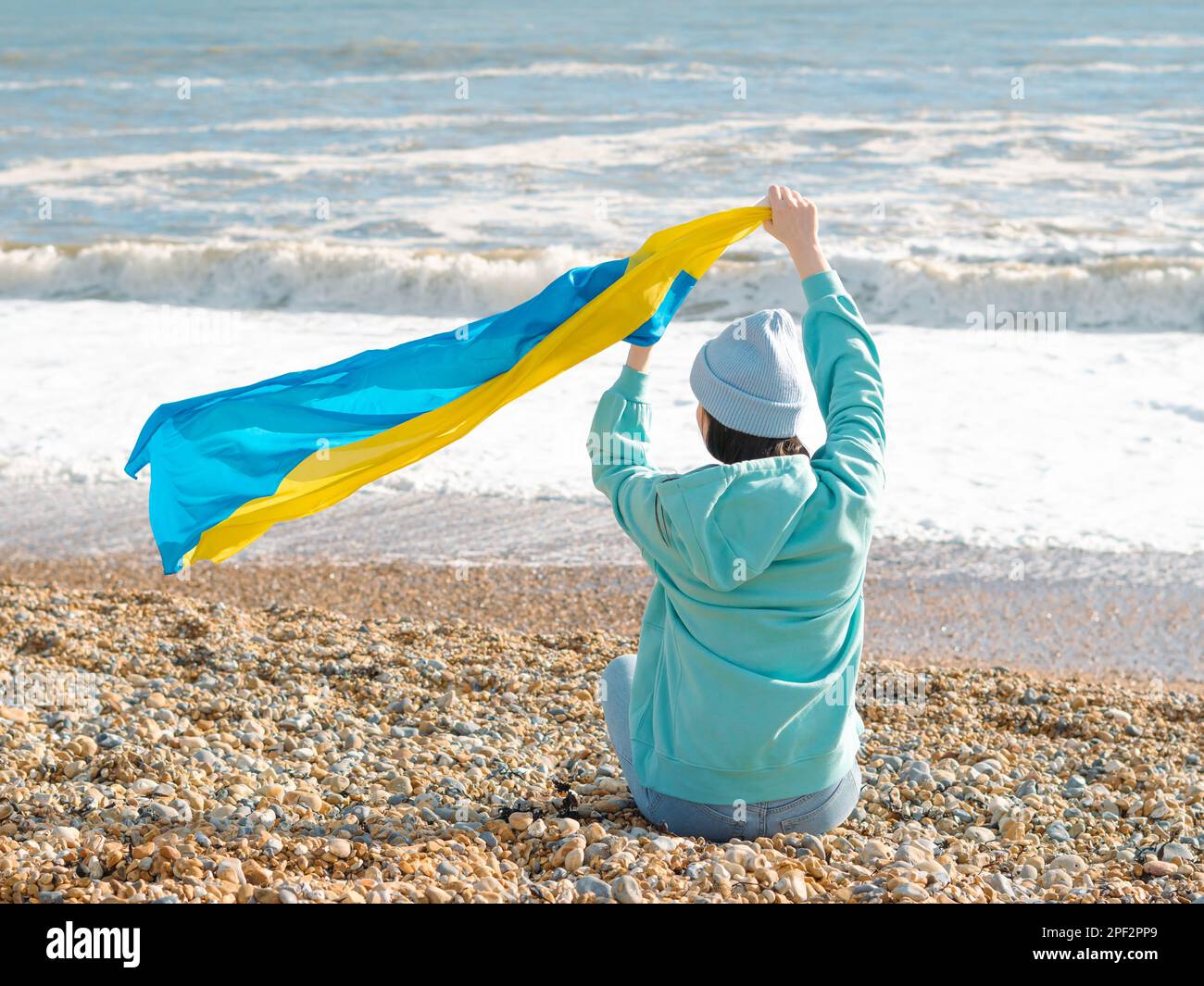 Braune Frau in blauem Hoodie und blauem Hut mit ukrainischer Nationalflagge, patriotisches Konzept Stockfoto