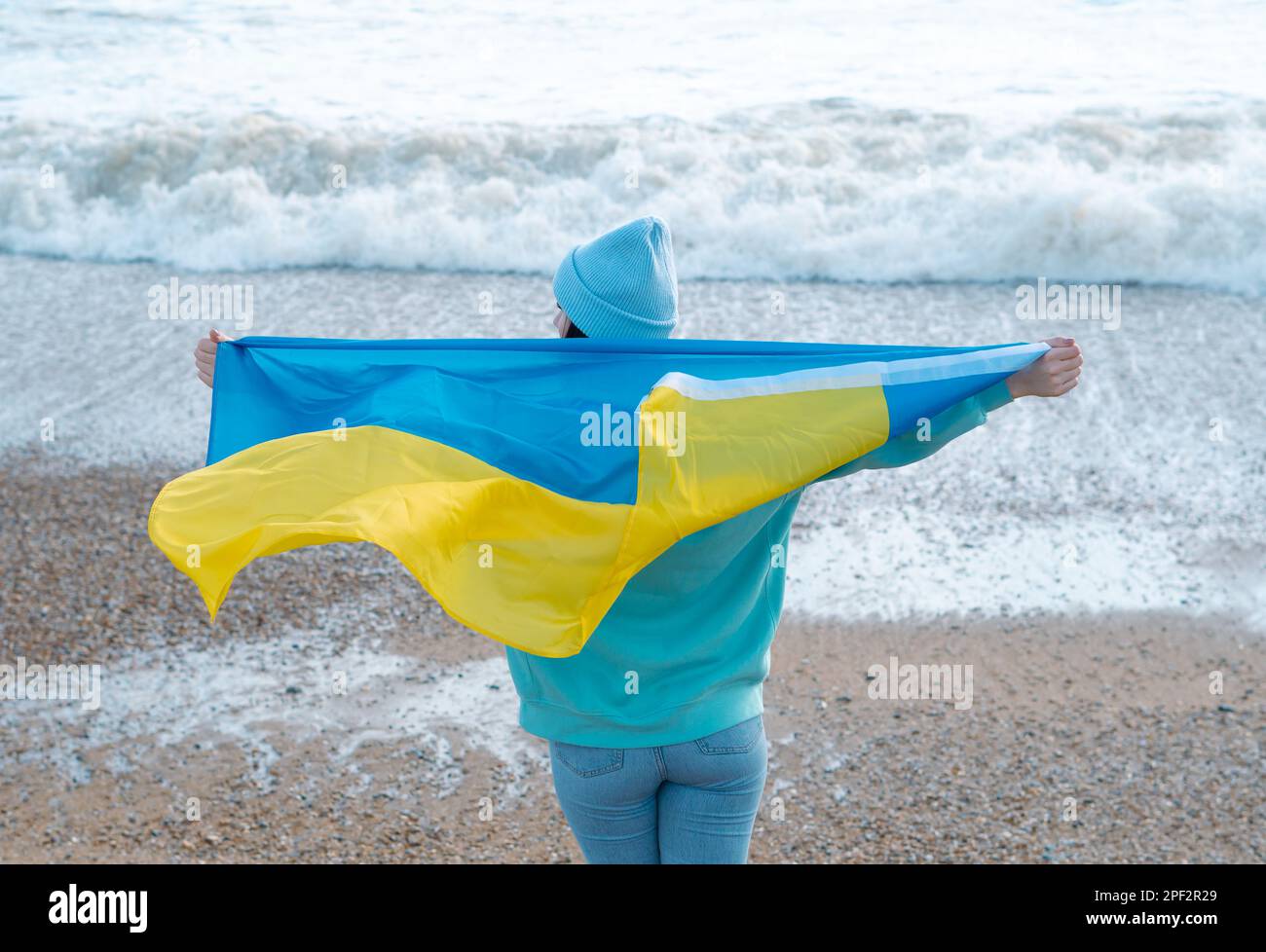 Braune Frau in blauem Hoodie und blauem Hut mit ukrainischer Nationalflagge, patriotisches Konzept Stockfoto