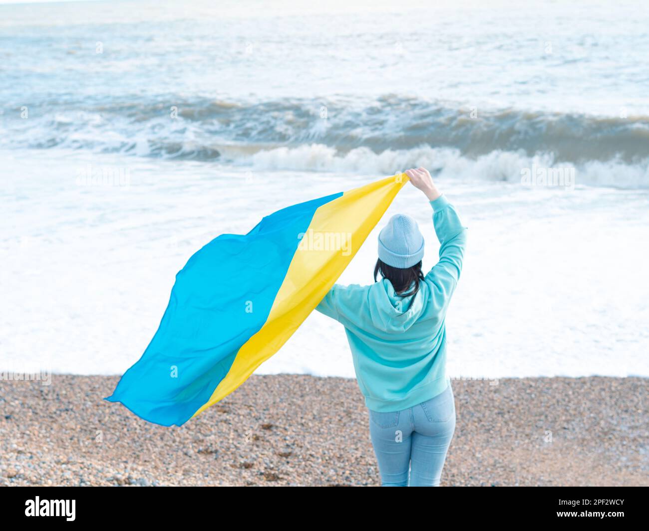 Braune Frau in blauem Hoodie und blauem Hut mit ukrainischer Nationalflagge, patriotisches Konzept Stockfoto