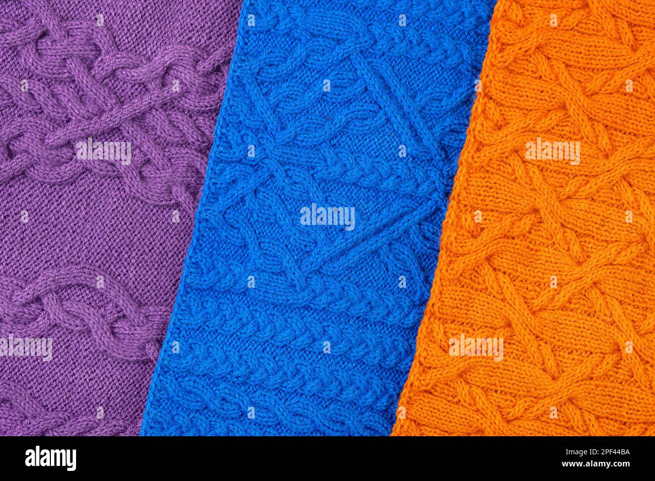 Gestrickter Hintergrund in Blau, Lila und Orange. Großer Strickstoff mit Muster. Nahaufnahme einer Strickdecke. Banner Stockfoto