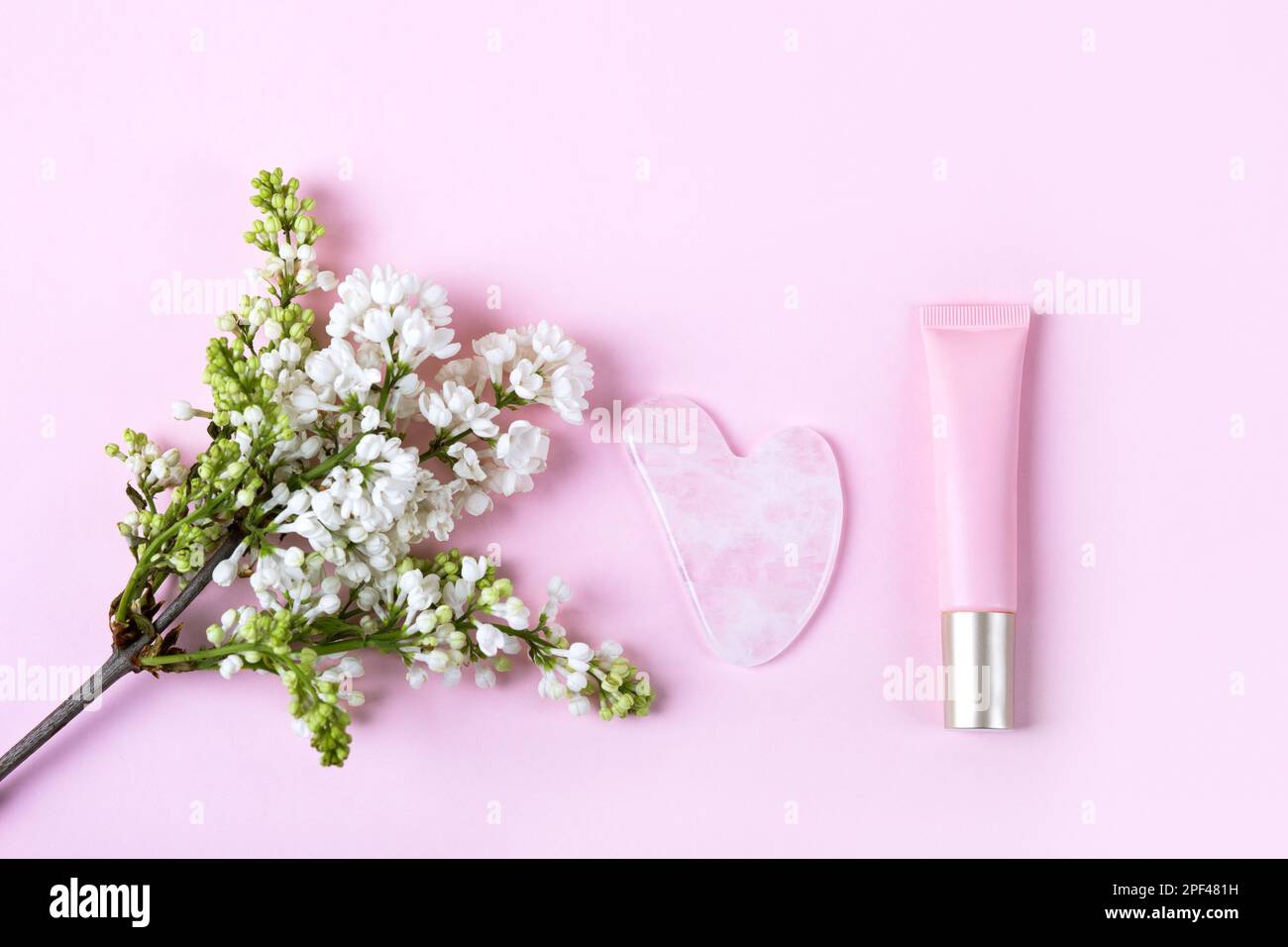 Kosmetikflasche und Gua-Sha für Gesichtsmassage mit Blumen Flieder. Massagegeräte für das Gesicht. Anti-Alters-, Hebe- und Tonpflegeprodukte. Moderne Selbstpflege Stockfoto