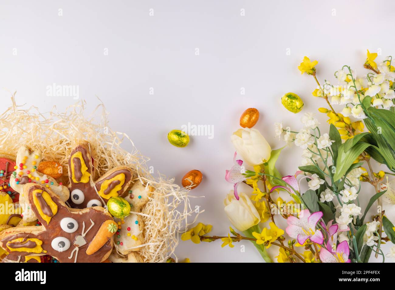 Farbenfroh dekorierte Osterkekse in einem Nest, Frühlingsblumen, Schokoladeneier, weißer Hintergrund Stockfoto