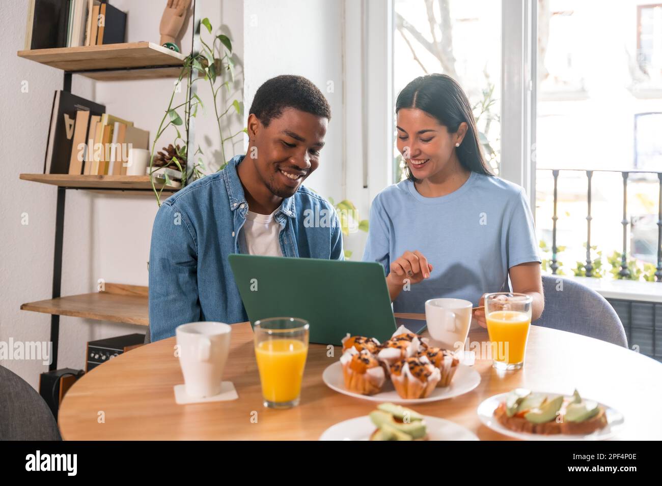 Multiethnisches Paar, das beim Frühstück online mit dem Computer einkauft Stockfoto