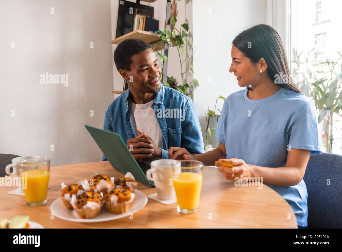Ein multiethnisches Paar kauft online mit dem Computer, während es frühstückt, direkt am Fenster Stockfoto