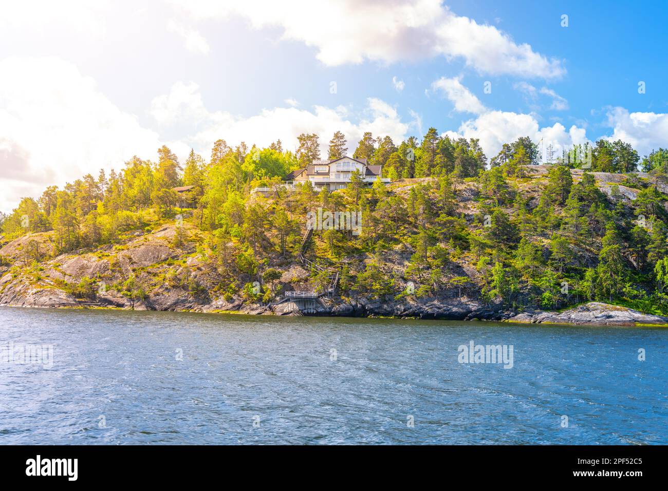 Edle ländliche Villa auf einem bewaldeten Hügel über einer Bucht an einem klaren Sommertag. Blick vom Meer. Stockholmer Archipel, Schweden Stockfoto