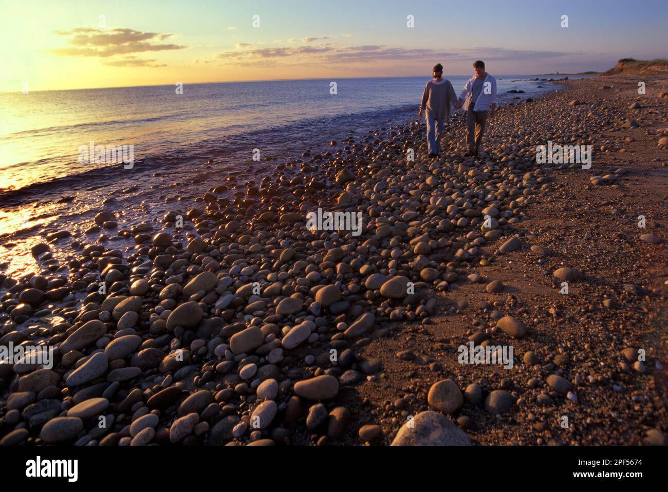 Ein junges Paar, das am irakischen Ufer spaziert und bei Sonnenuntergang Händchen hält Stockfoto