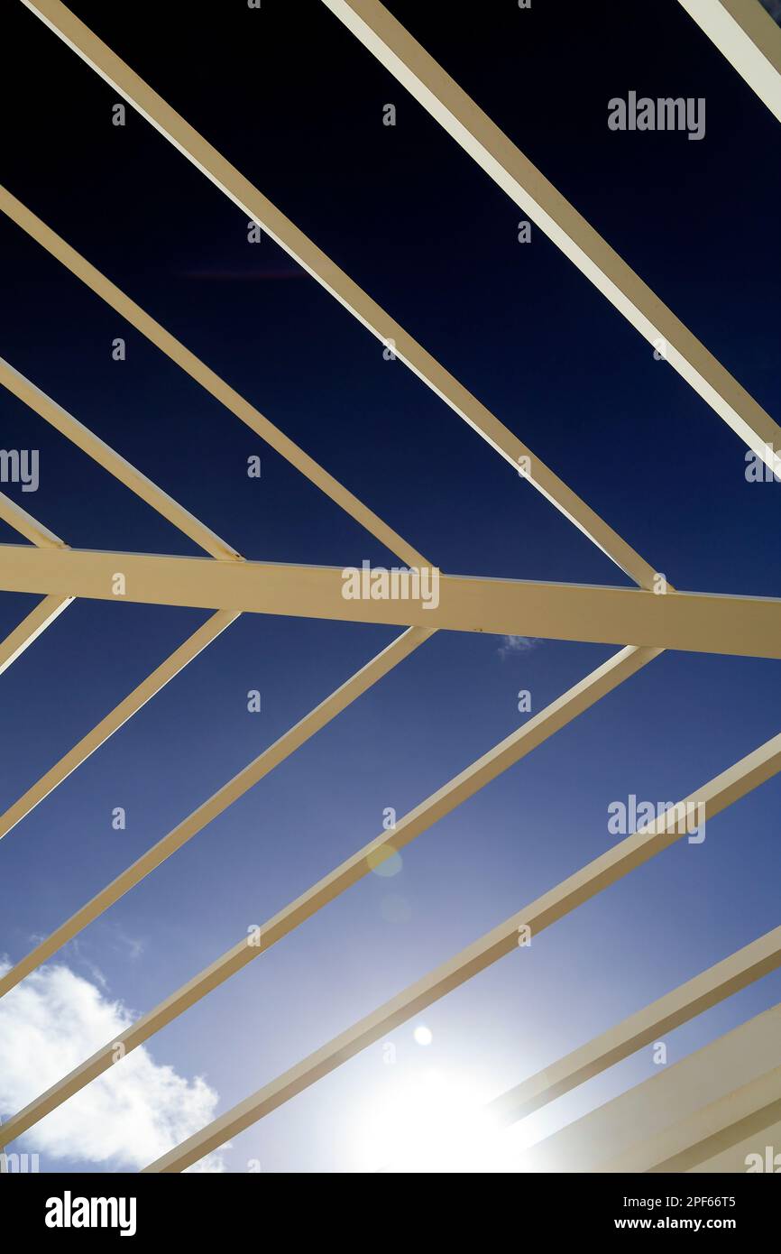 Blauer Himmel, Sonne und Wolken durch den Rahmen einer Pergola. Abstrakte Muster, Licht und Schatten. Zyl Stockfoto