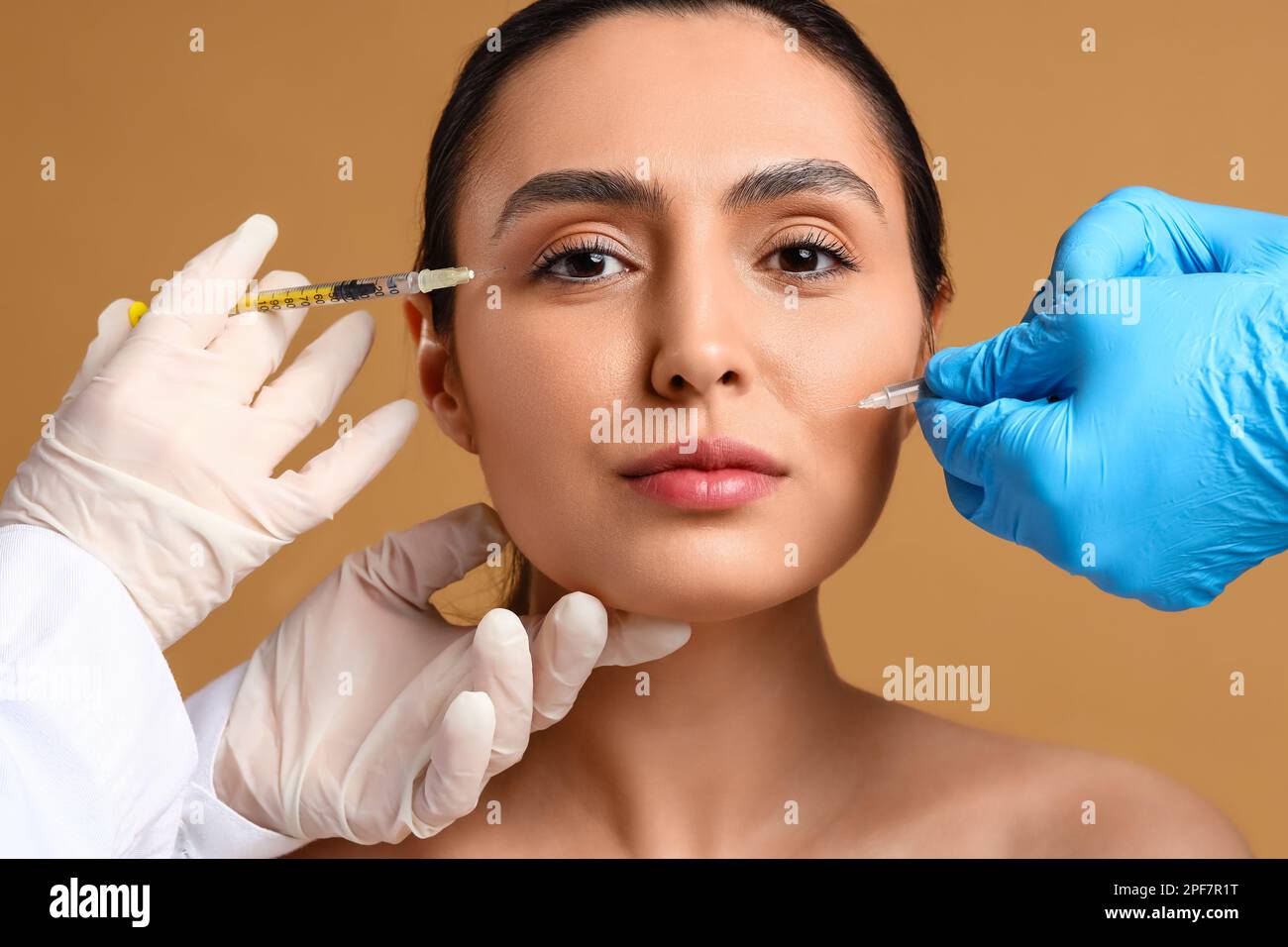 Junge Frau, die Füllstoffinjektionen im Gesicht vor beigem Hintergrund erhält Stockfoto