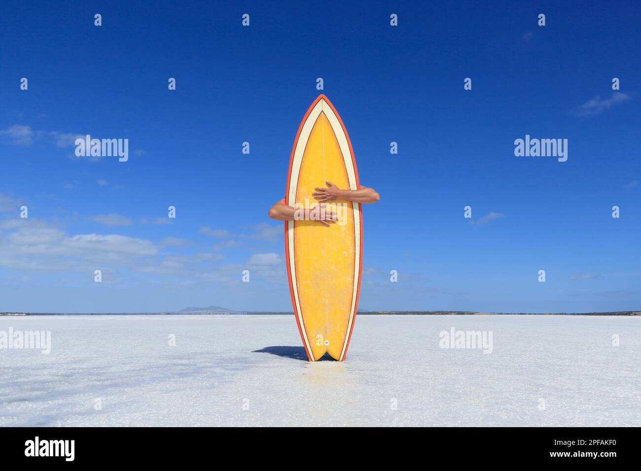 Person, die ein gelbes Surfbrett auf einem Salzsee umarmt. Stockfoto