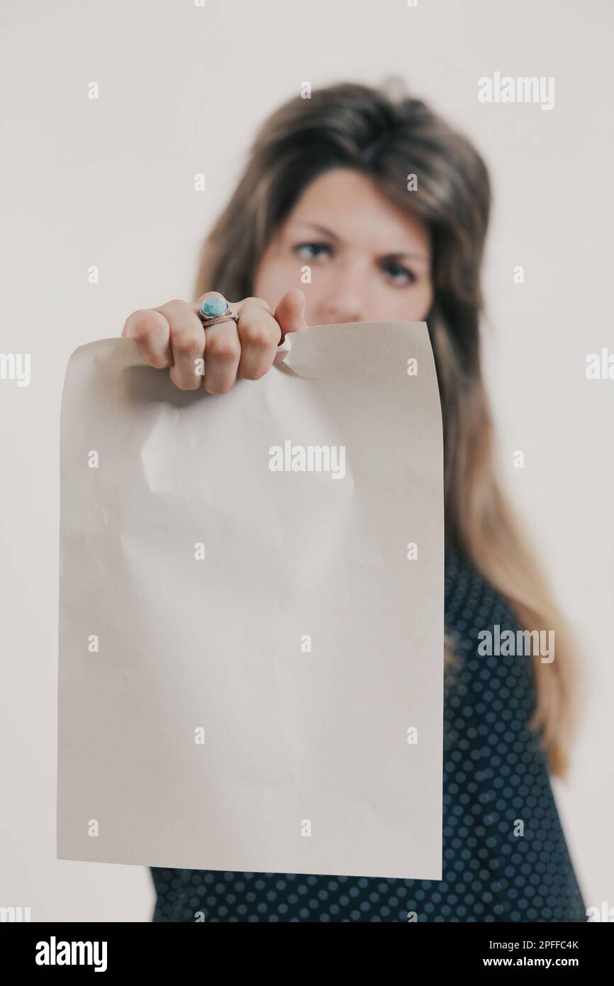 Leeres, von einer weiblichen Hand gehaltenes Blatt mit Ring im Vordergrund. Die Hand ist von einer Frau mit langen Haaren und einem runzelnden Blick, die ein langes dunkles Kleid trägt. Stockfoto