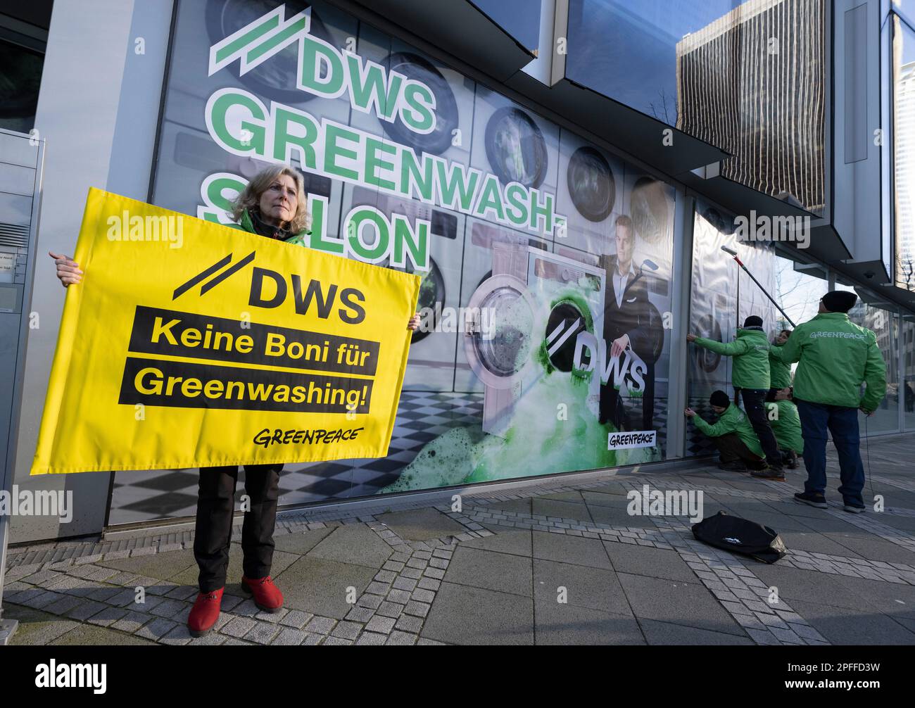 16. März 2023, Hessen, Frankfurt/Main: Aktivisten von Greenpeace bedecken die Glasfassade der DWS-Tochtergesellschaft der Deutschen Bank in Frankfurt mit Bildern eines „Waschsalons“. Damit wollen die Aktivisten gegen die Nachhaltigkeitspolitik von DWS und die Boni für CEO Stefan Hoops protestieren (direkt auf dem Poster). Foto: Boris Roessler/dpa Stockfoto
