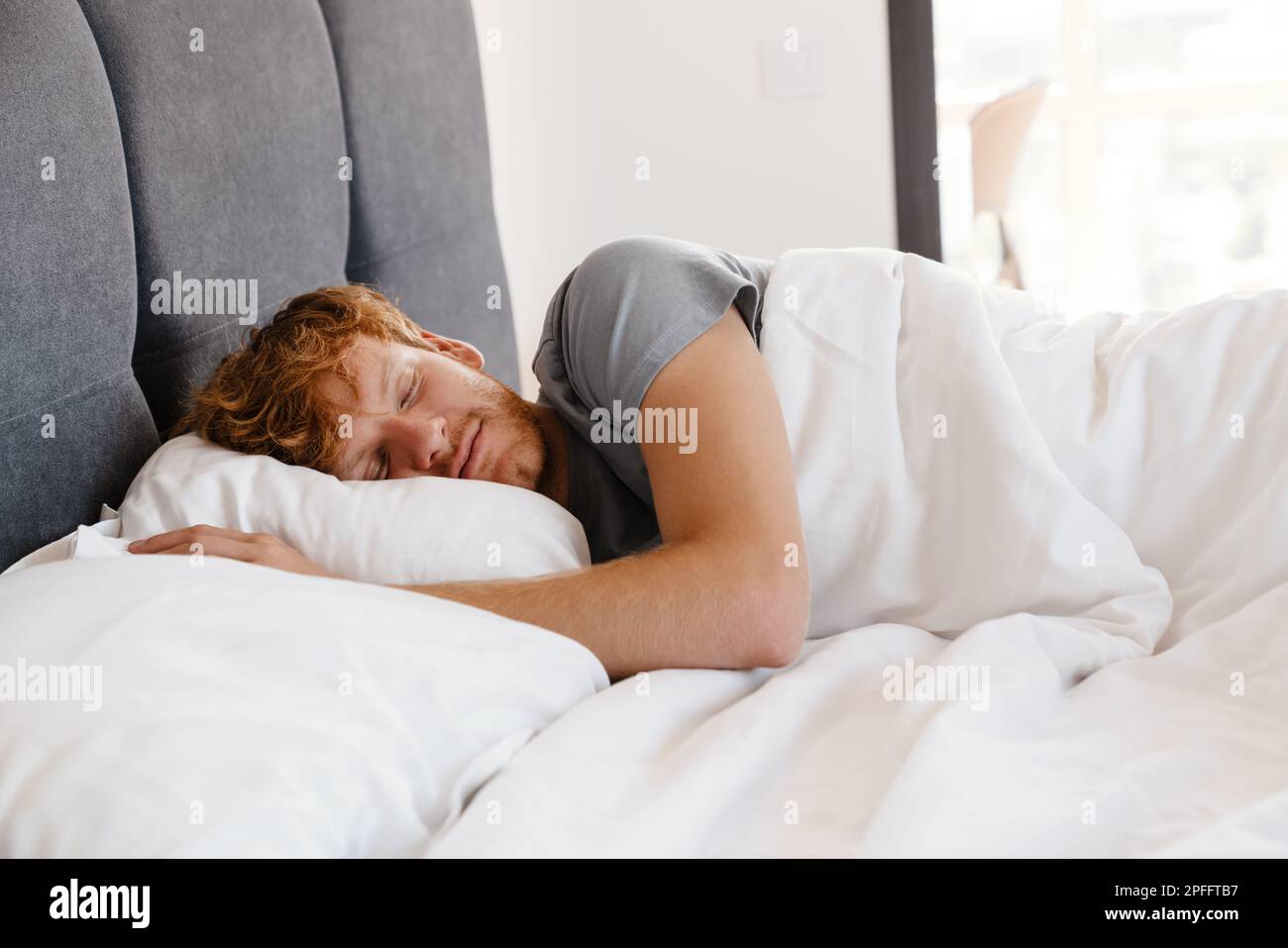 Porträt eines jungen, attraktiven, schlafenden Rothaarigen im grauen T-Shirt zu Hause im Bett Stockfoto