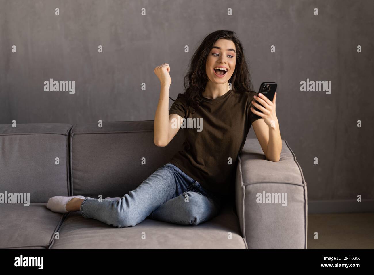 Aufgeregt Frau Erfolge feiern Holding Handy sitzen auf einer Couch in der Nacht zu Hause Stockfoto