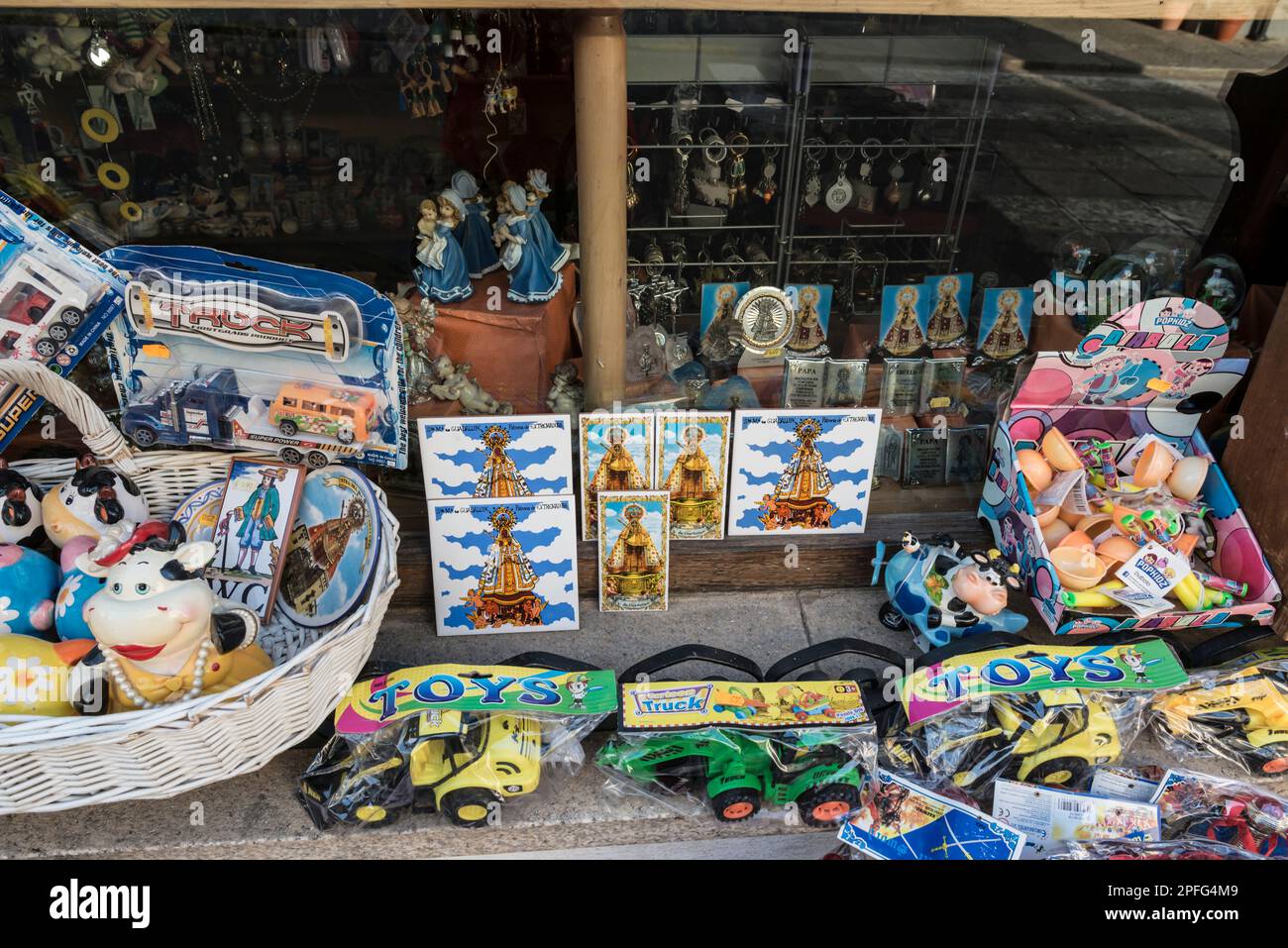 Religiöse Souvenirs in einem Schaufenster von „Our Lady of Guadalupe“ unter Spielzeug in einem Souvenirladen. Guadalupe, Provinz Caceres, Extremadura, Spanien. Stockfoto