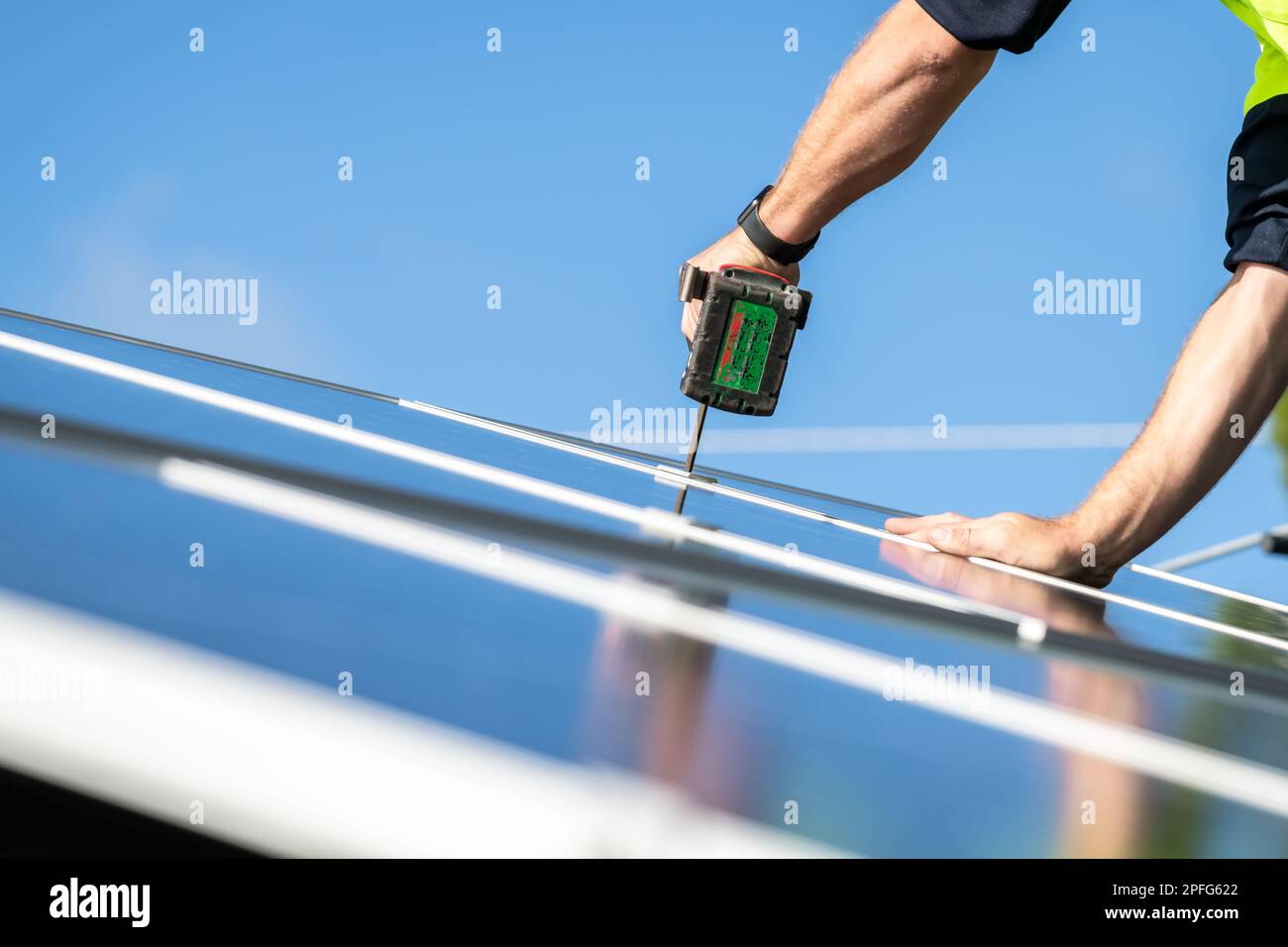 Nicht identifizierter Elektriker, der Solarpaneele auf dem Hausdach mit einem Akkuschrauber installiert Stockfoto