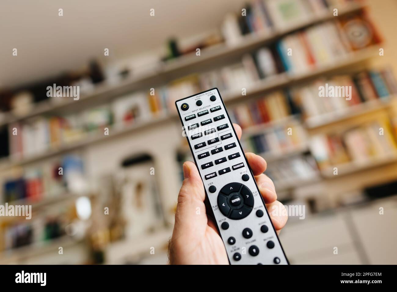 Frankfurt, Deutschland - 23. Februar 2023: Nahaufnahme POV männliche Hand mit neuer Fernsteuerung Onkyo RC-816C mit USB NET, CD, Phono und anderen Knöpfen im Wohnzimmer mit Vitsoe-Regalen im Hintergrund Stockfoto