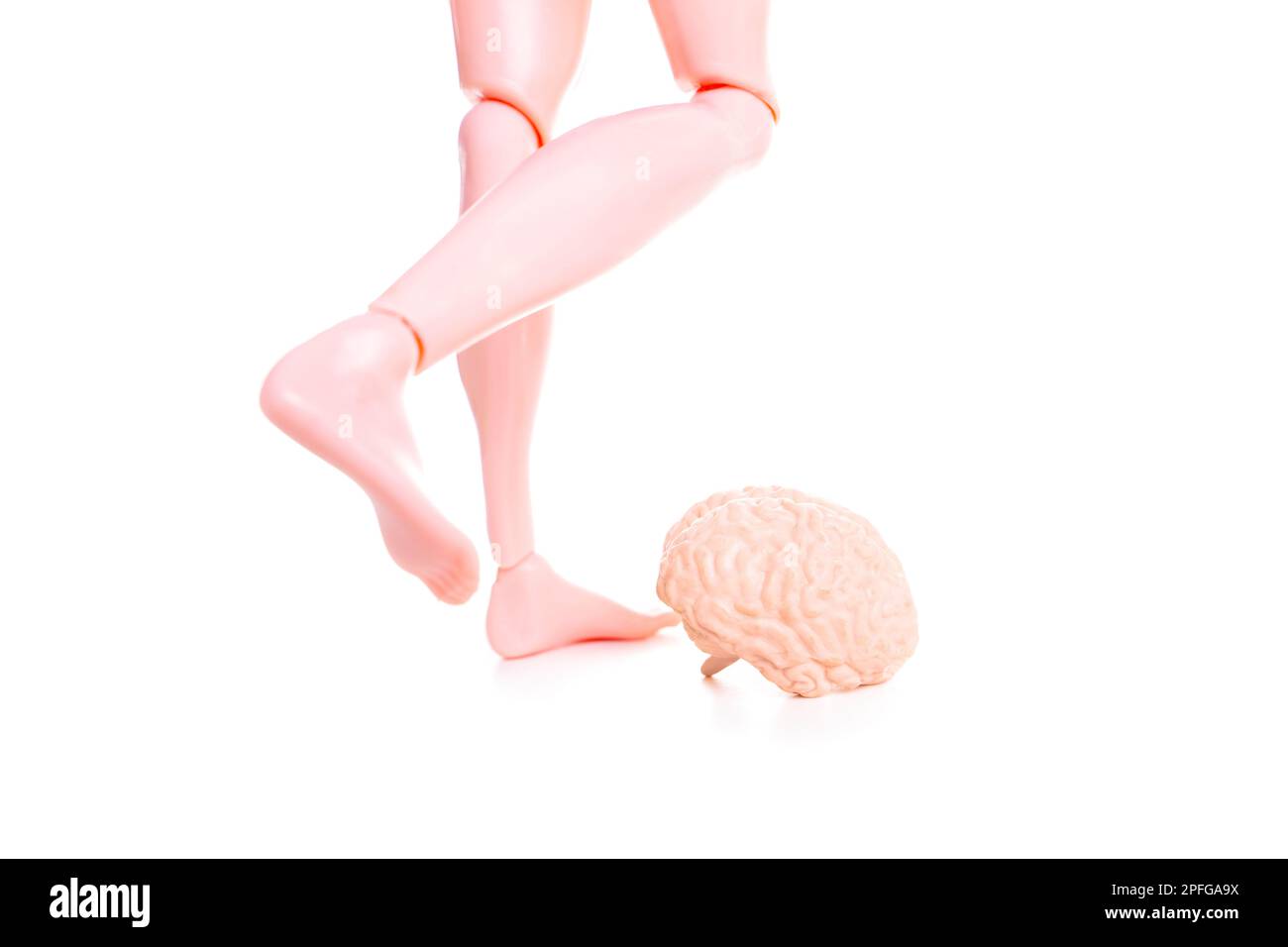 Die Spielzeugpuppe zieht sich zusammen, um ein kleines menschliches Gehirnmodell wie einen Fußball zu treten. Komisches Konzept, die Kontrolle über den Verstand zu übernehmen und negativ zu „treten“ Stockfoto