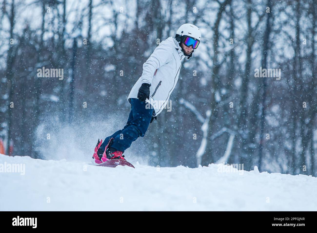 Snowboard-Mann, der bergab mit Schneewittchen fährt. Männerritt auf Snowboard in den Bergen. Aktiver Mann mit Schutzhelm, Schutzbrille und Skistöcken beim Laufen Stockfoto