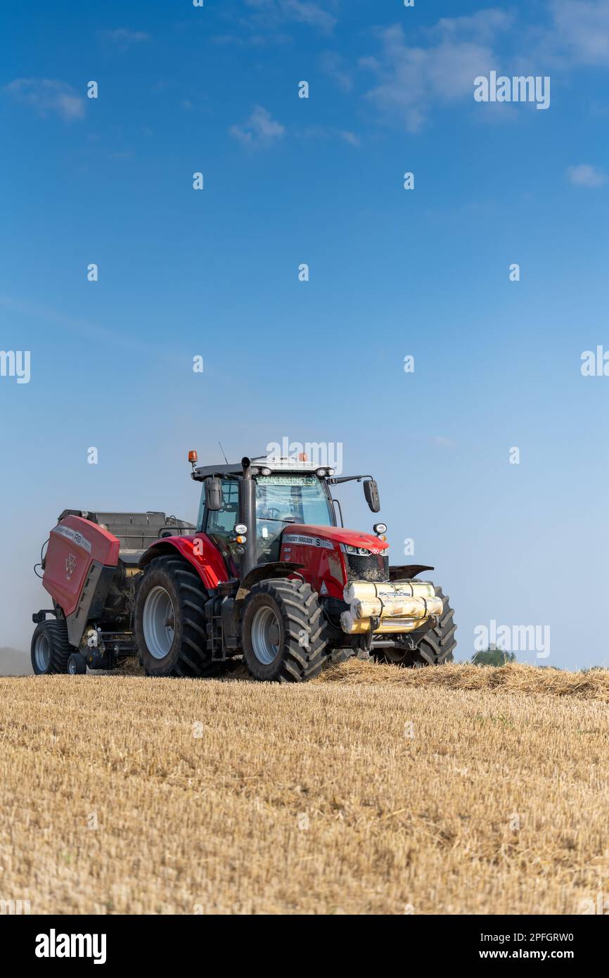 Pressen von Stroh zu Rundballen mit einem Massey Ferguson-Traktor 7726 und einer Ballenpresse RB4160v. Der Strohhalm wird als Tiereinstreu verwendet. North Yorkshire, Großbritannien. Stockfoto