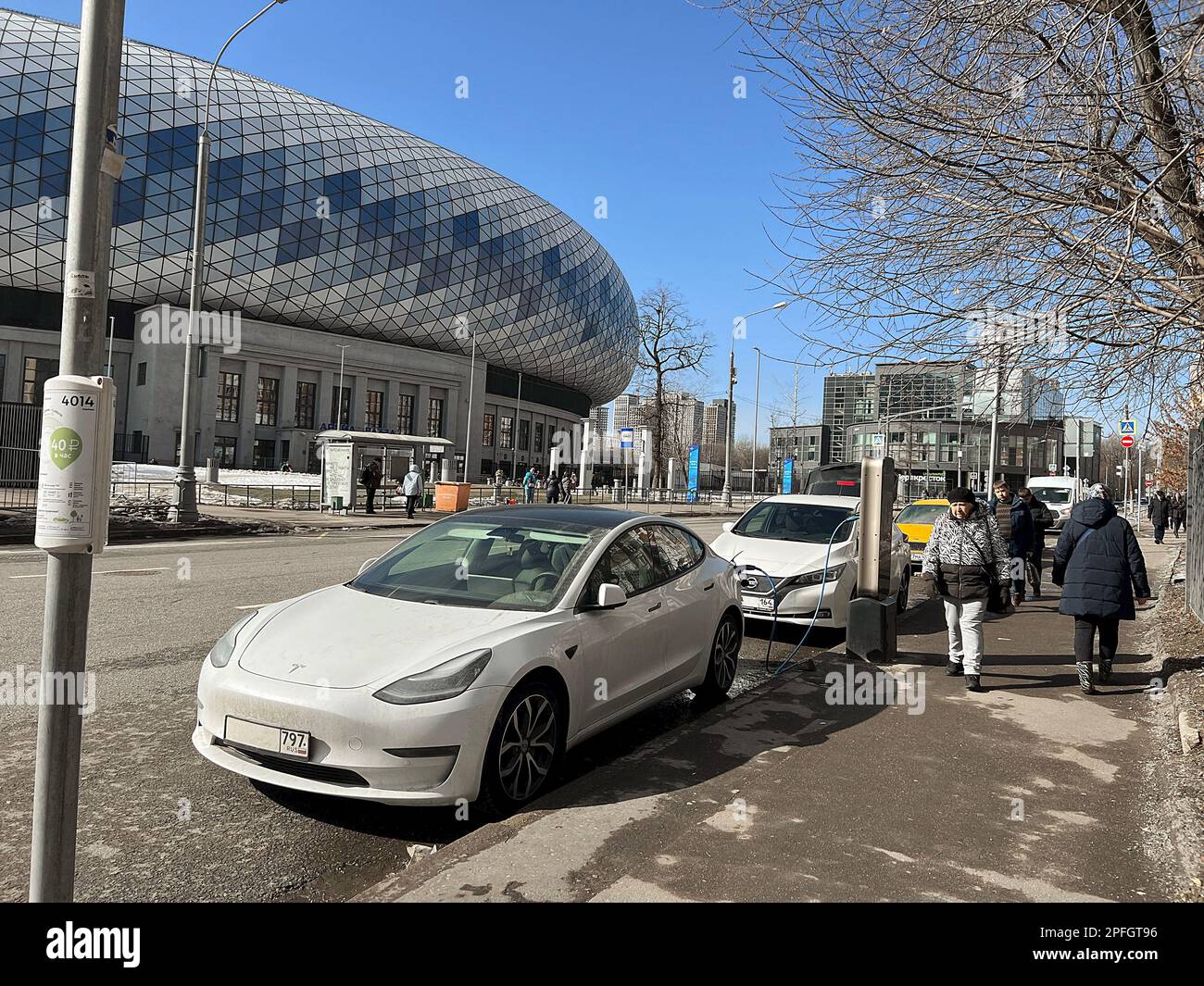 Moskau, Russland - 17. März 2023: Aufladen von Tesla Elektroautos auf kostenlosen Parkplätzen in der Nähe eines modernen neuen Stadions. Elektroauto. Stockfoto