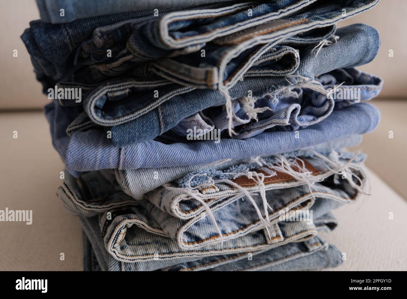 Gefaltete Jeans, ein Stapel Jeans in verschiedenen Farben auf einem weißen Sofa. Gefaltete Jeanshosen in einer Reihe auf einem weißen Sessel. Konzeptidee. Stockfoto