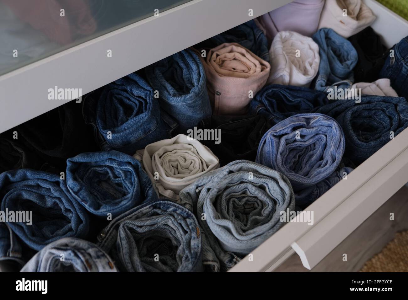 Schublade voll mit Jeanshosen, offene Schublade mit gefalteten Jeans drinnen. Konzeptfoto mit diagonalem Rahmen. Stockfoto