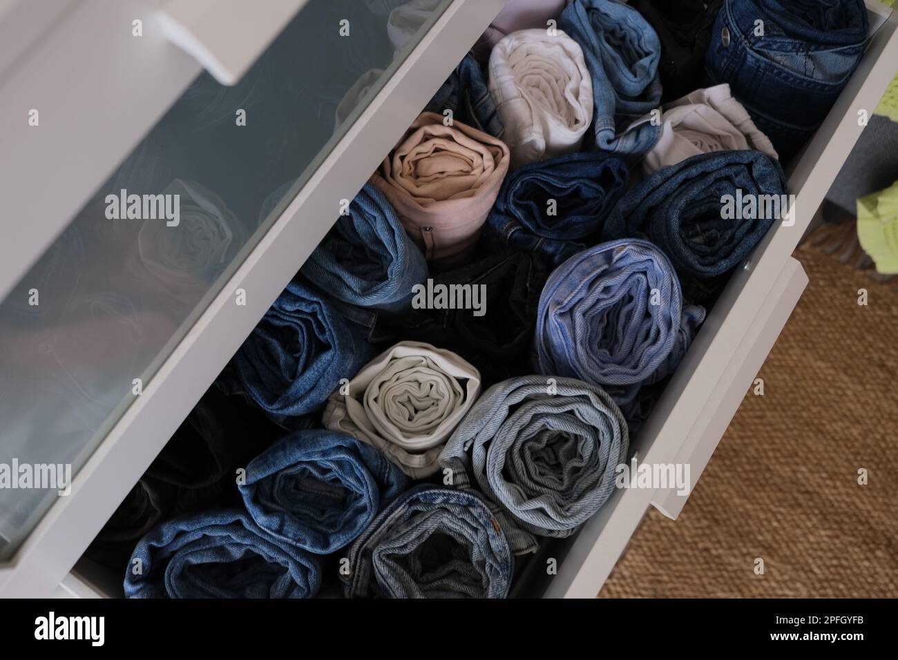 Kommode voll mit gerolltem Denim, offener Schubladenstapel mit gerollten Jeans Hosen drinnen, Nahaufnahme. Konzeptfoto mit diagonalem Rahmen. Stockfoto