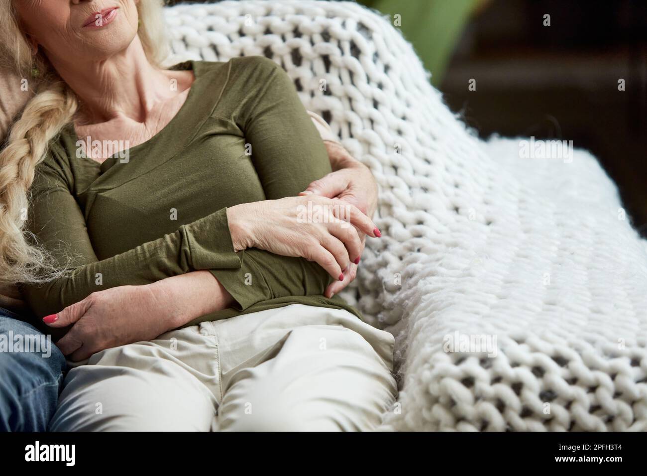Zugeschnittenes Bild einer Seniorin, Frau, die mit ihrem Mann auf der Couch sitzt und sie umarmt, unterstützt und aufmerksam macht. Gemütlichkeit Stockfoto