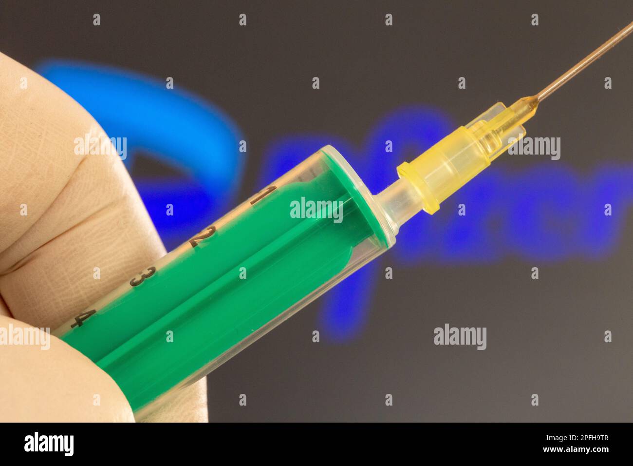 Symbolbild Corona Vaccination/Pfizer: Nahaufnahme einer Injektionsnadel, Pfizer-Logo im Hintergrund. Die Debatte über mögliche Impfschäden ist Cu Stockfoto