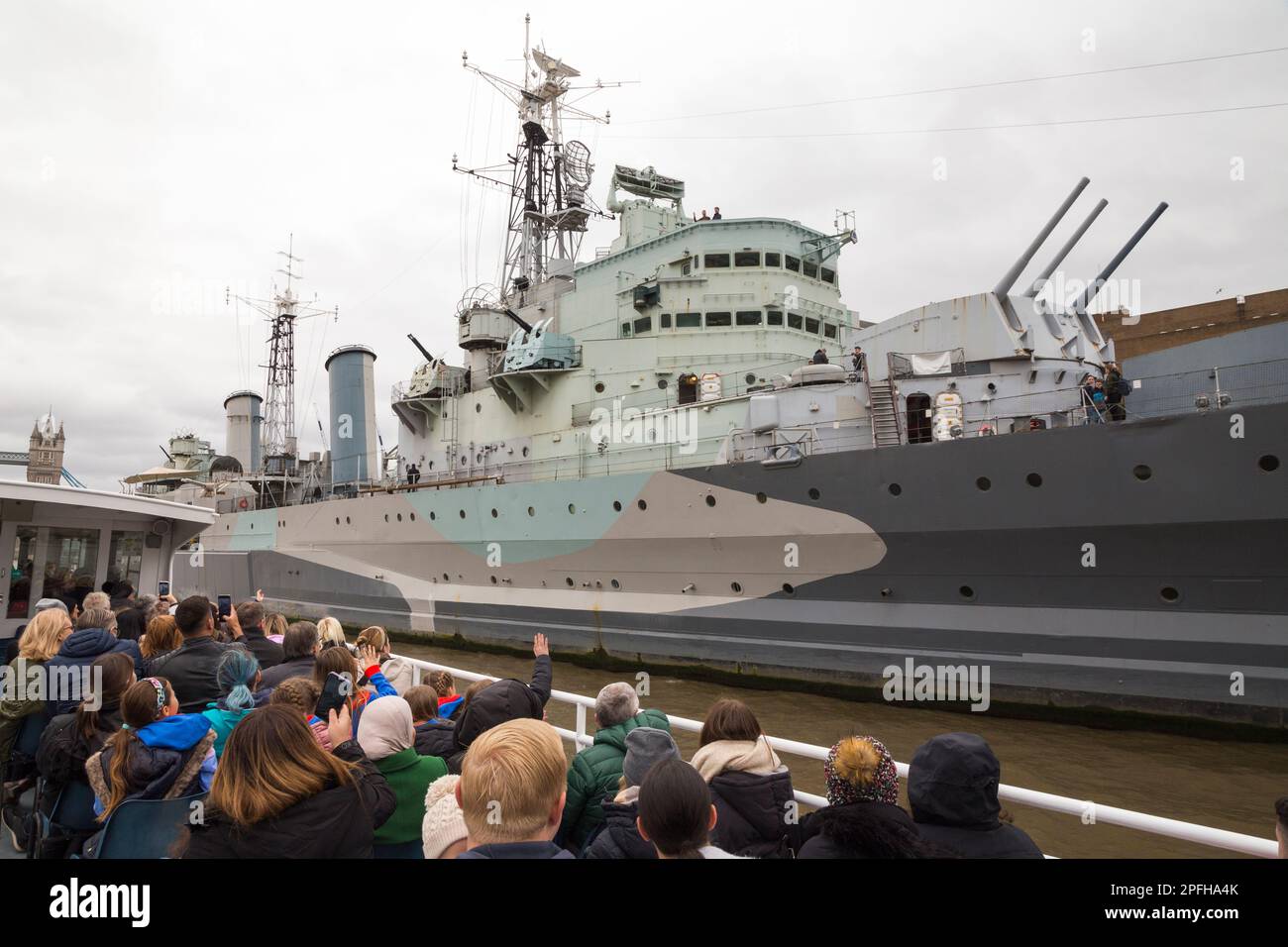 Touristenboot komplett mit Touristen, die HMS Belfast sehen, ein leichtes Kreuzfahrtschiff der Stadtklasse, gebaut für die Royal Navy. Jetzt dauerhaft als Museumsschiff auf der Themse in London, Großbritannien, festgemacht. (133) Stockfoto