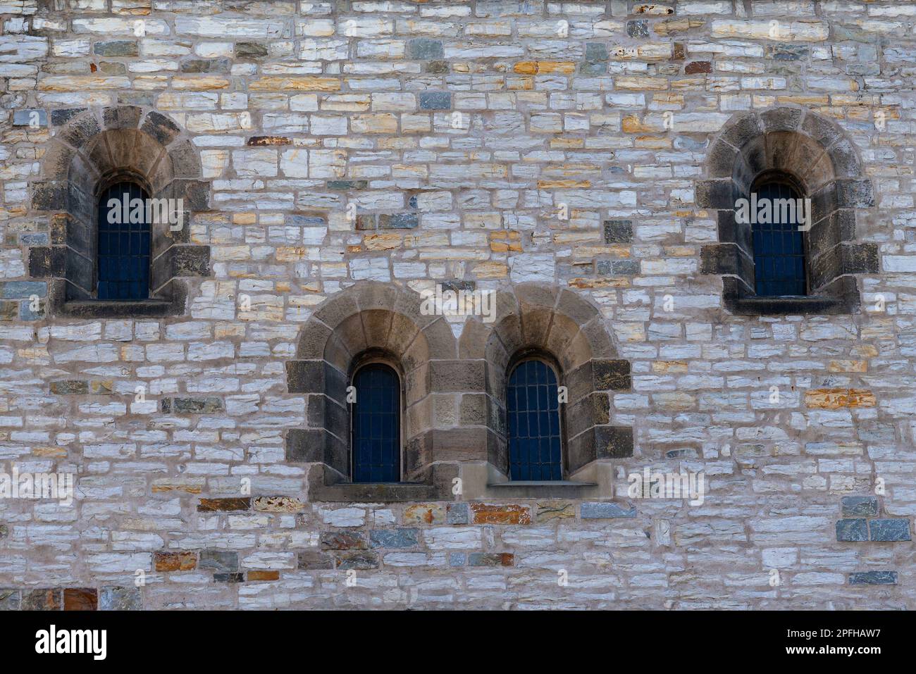 Steinwand eines alten Gebäudes mit Bogenfenstern. Alte antike Kirche. Vier Fenster sind mit Metallgitter verschlossen. Stockfoto Steinwand eines alten Gebäudes mit Bogenfenstern. Alte antike Kirche. Vier Fenster sind mit Metallgitter verschlossen. Stockfoto
