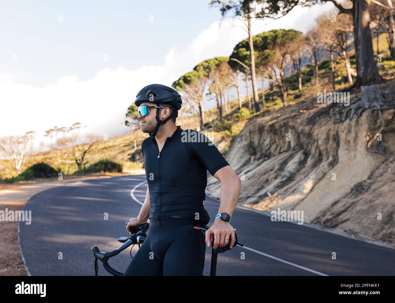 Seitenansicht eines professionellen Motorradfahrers, der sich auf seinem Road Bike entspannt. Männlicher Radfahrer mit Brille und Helm genießt die Aussicht und macht eine Pause während der Stockfoto