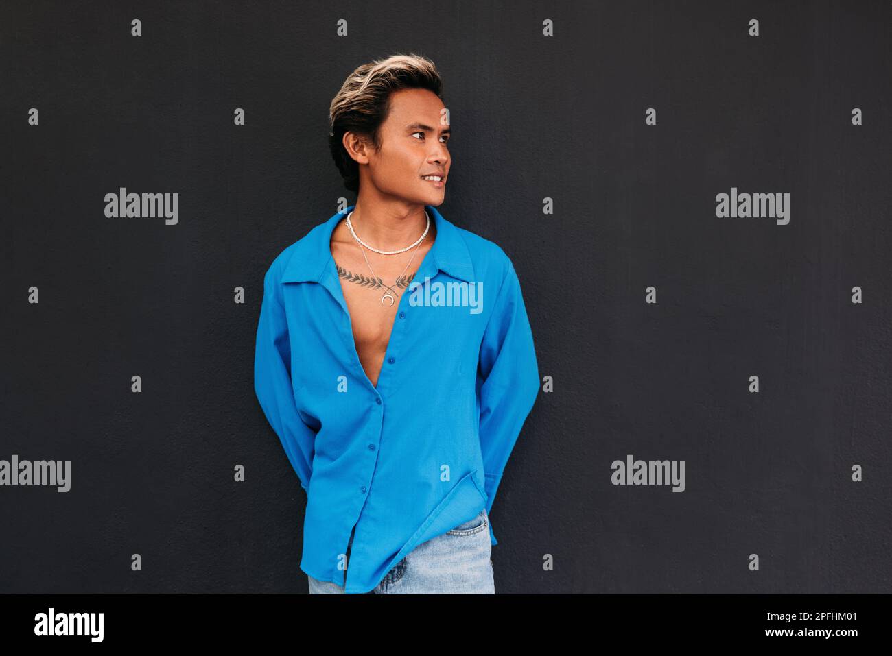 Junger, stylischer Typ in blauem Hemd, der an der schwarzen Wand posiert Stockfoto