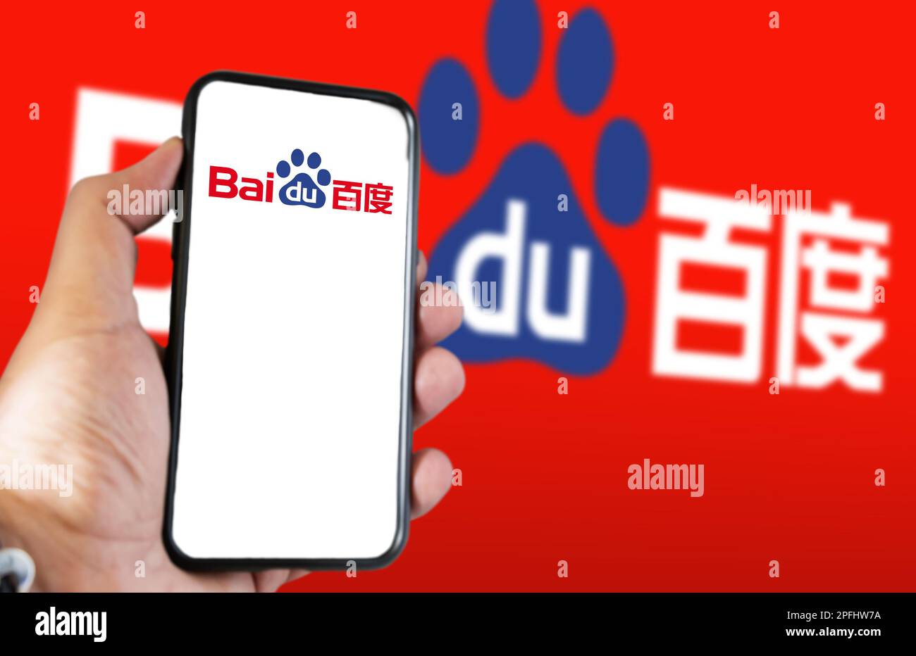 Peking, CN, Februar 2023: Eine Hand, die ein Telefon hält und die Baidu-Website auf dem Bildschirm angezeigt wird. Roter Hintergrund mit verschwommenem Baidu-Logo. Baidu ist ein chinesischer Multina Stockfoto