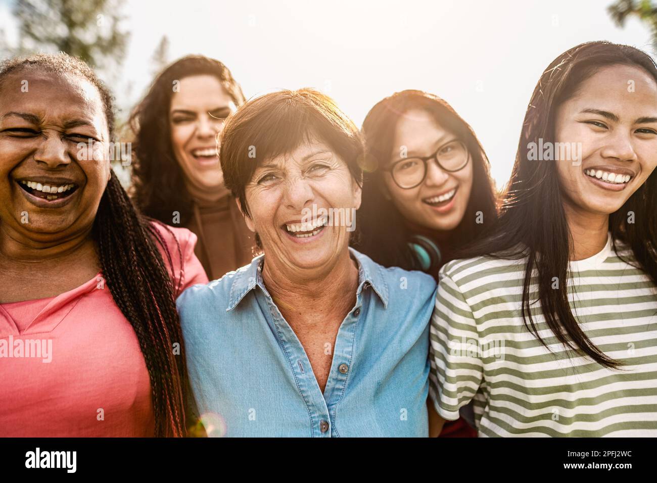 Glückliche Frauen aus mehreren Generationen mit unterschiedlichem Alter und unterschiedlicher ethnischer Zugehörigkeit, die in einem öffentlichen Park vor der Kamera lächeln Stockfoto
